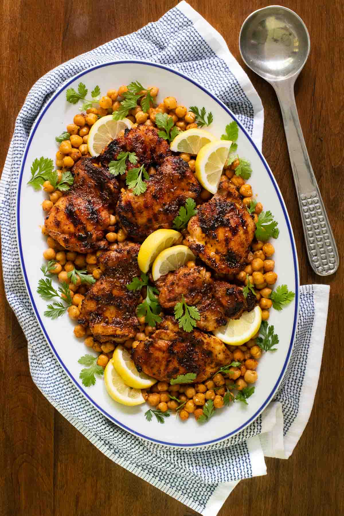 Overhead vertical photo of a presentation platter filled with Charred Honey Lemon Grilled Chicken with Crispy Chickpeas in a blue and white serving platter on a wood table.