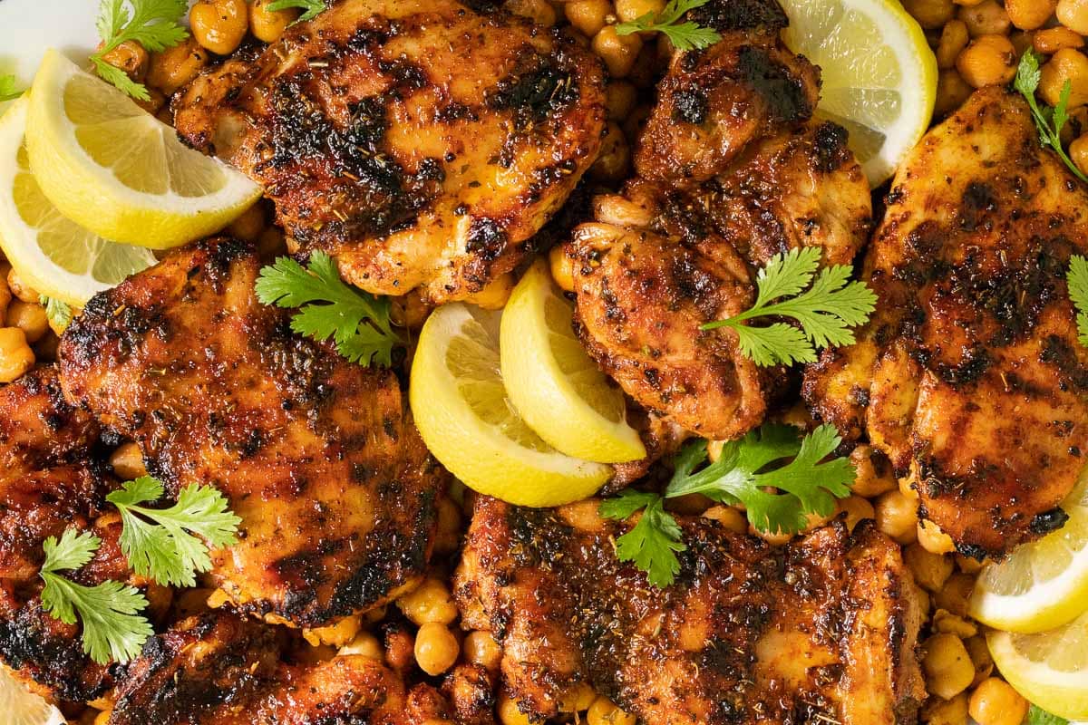 Vertical closeup photo of a plate of Charred Honey Lemon Grilled Chicken with Crispy Chickpeas garnished with cilantro and lemon wedges.