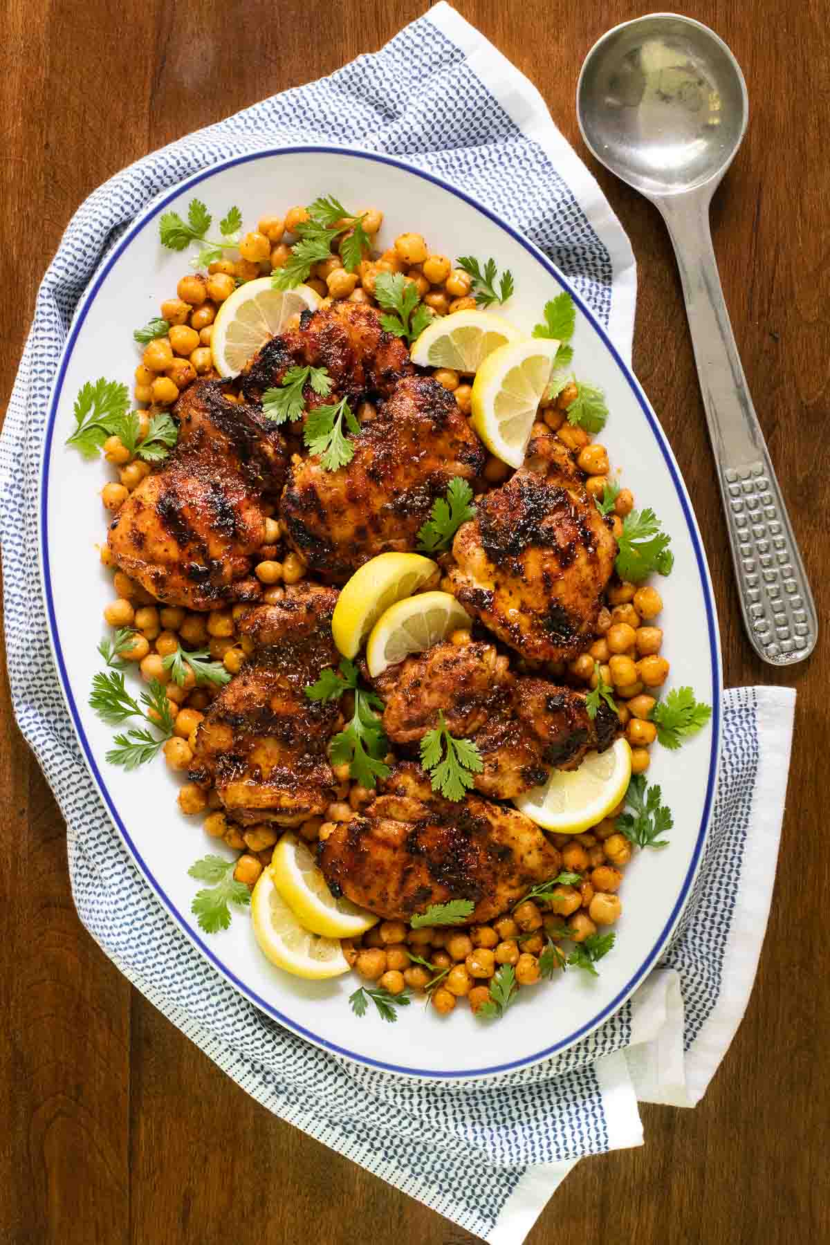 Overhead vertical photo of a serving plate of Charred Honey Lemon Grilled Chicken with Crispy Chickpeas on a wood table.