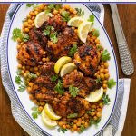 Overhead vertical photo of a presentation platter filled with Charred Honey Lemon Grilled Chicken with Crispy Chickpeas on a wood table.