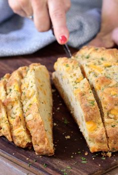 Vertical picture of cheddar herb Irish Soda bread cut into slices on a wooden cutting board