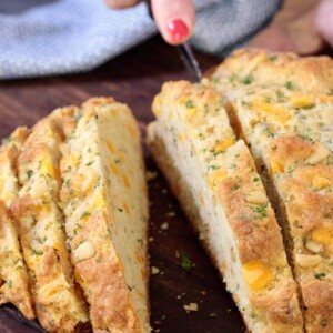 Vertical picture of cheddar herb Irish Soda bread cut into slices on a wooden cutting board