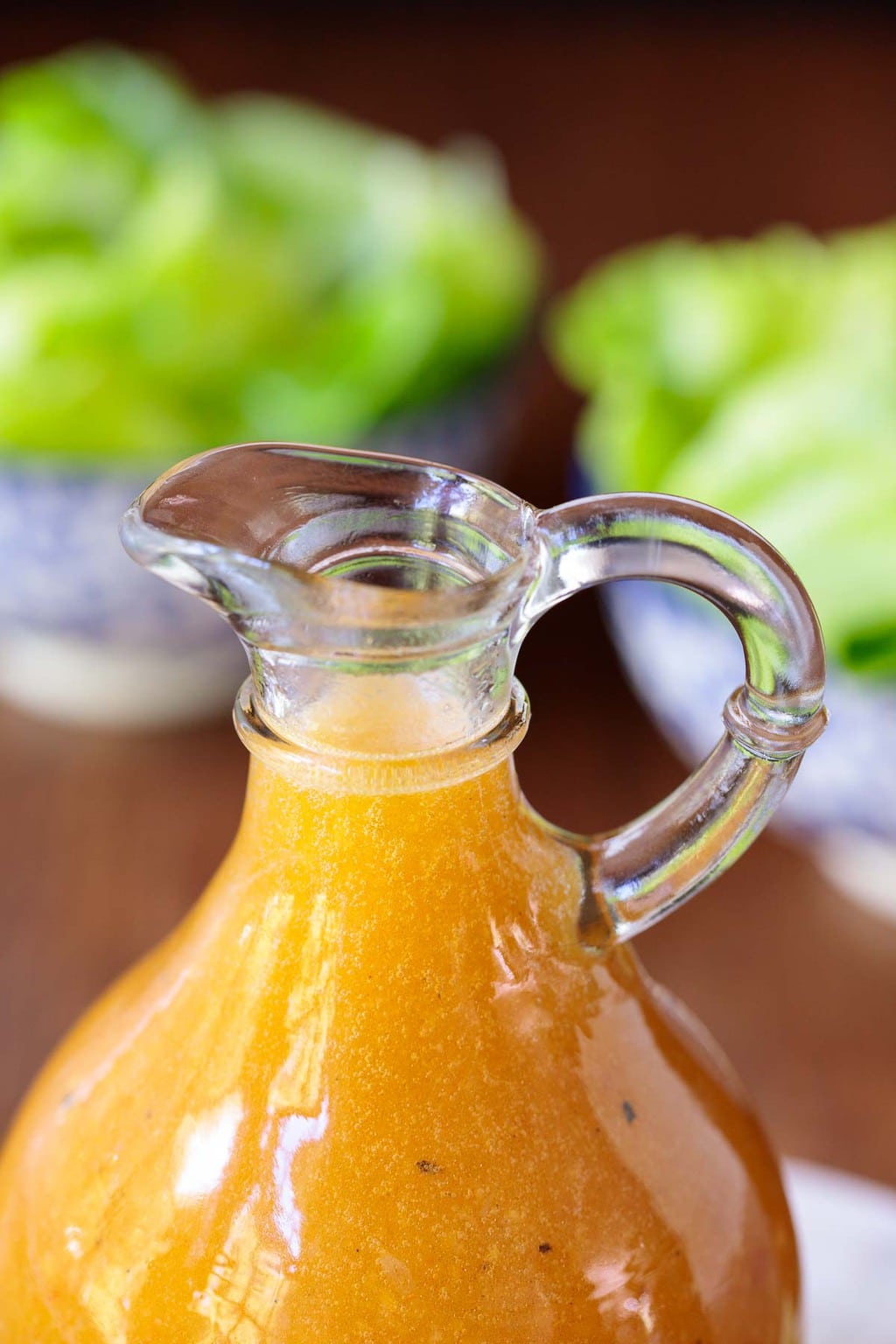 Closeup photo of a glass pitcher of Chili Lime Salad Dressing with bowls of salad in the background.
