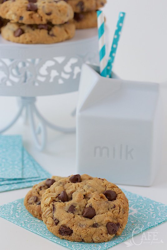 Photo of Chocolate Chip Cherry Oatmeal Cookies on a turquoise and white napkin with a milk container and a pedestal plate filled with more cookies.