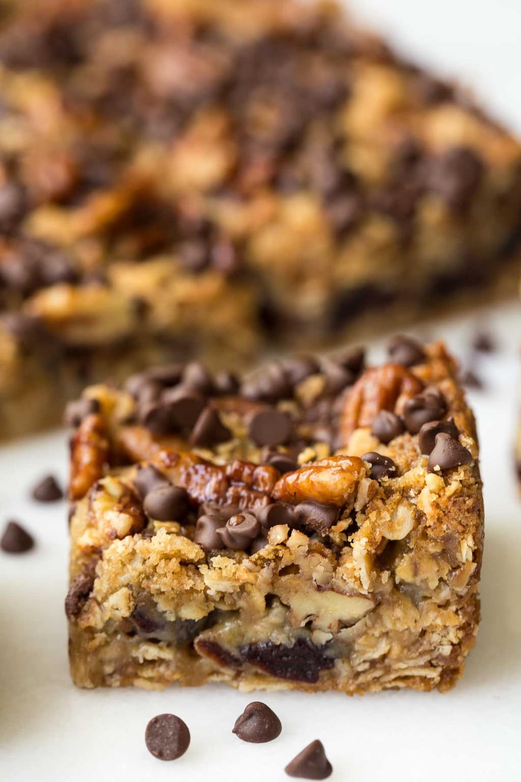 Closeup side photo of a Chocolate Chip Cherry Oatmeal Bar with a pan of the bars in the background.