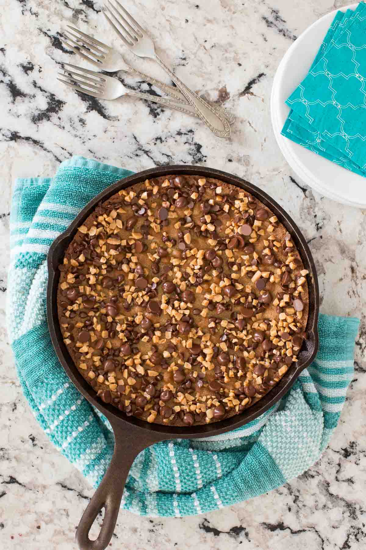 Overhead photo of a Chocolate Chip Toffee Skillet Tart nestled in a turquoise bowl on a black and white granite countertop.