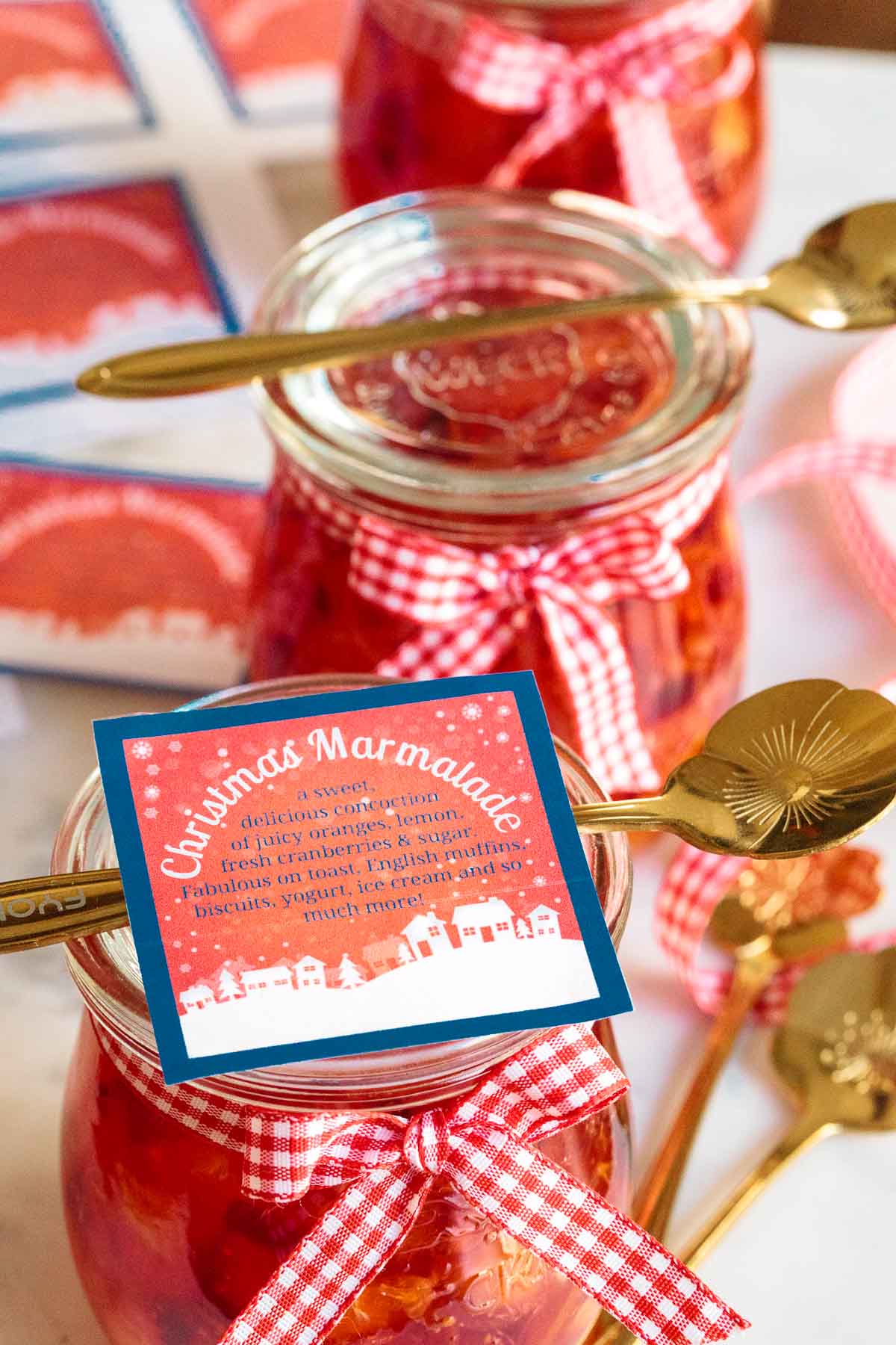 Photo of gift jars of Easy Orange-Cranberry Christmas Marmalade with gold serving spoons and labels on top of each jar.