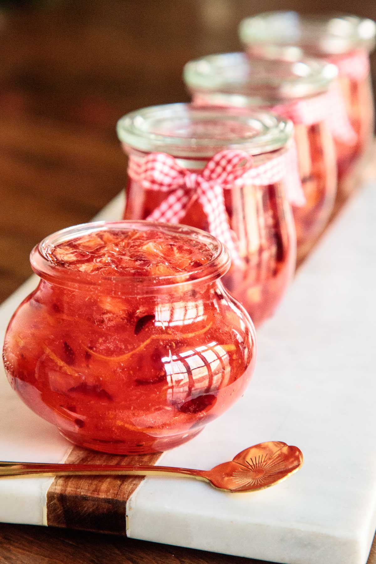 Vertical closeup photo of Easy Christmas Marmalade in glass Weck jars lined up on a marble tray.