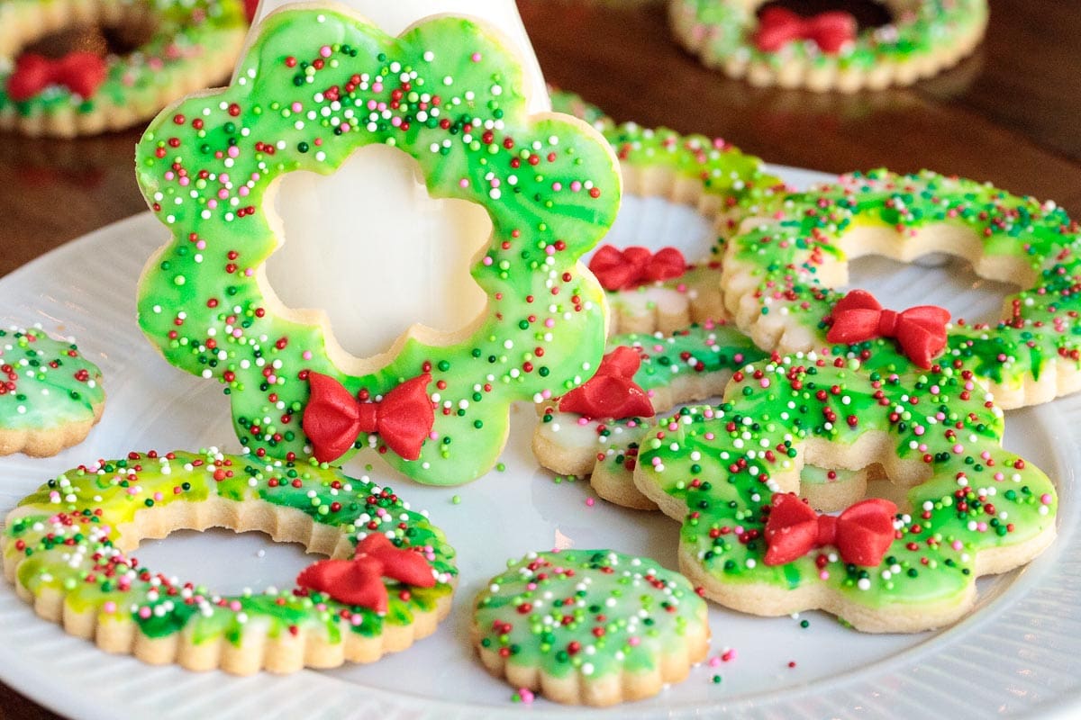 Photo of a white plate filled with Christmas Wreath Shortbread Cookies and a jar of milk.