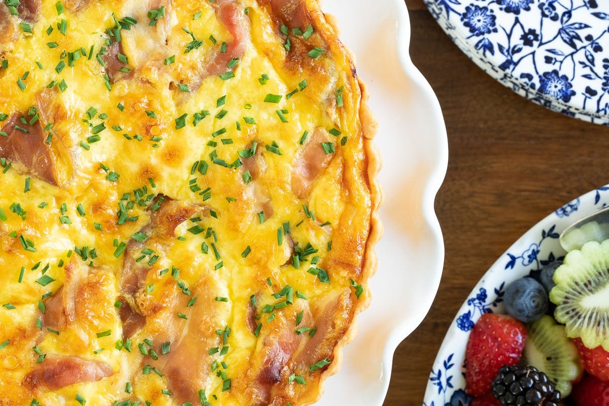 Horizontal closeup overhead photo of a Classic Quiche Lorraine with Prosciutto on a white serving dish