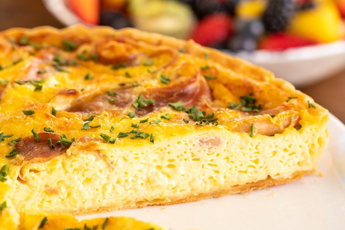 Horizontal closeup photo of the inside of a Classic Quiche Lorraine with Prosciutto on a white serving plate.