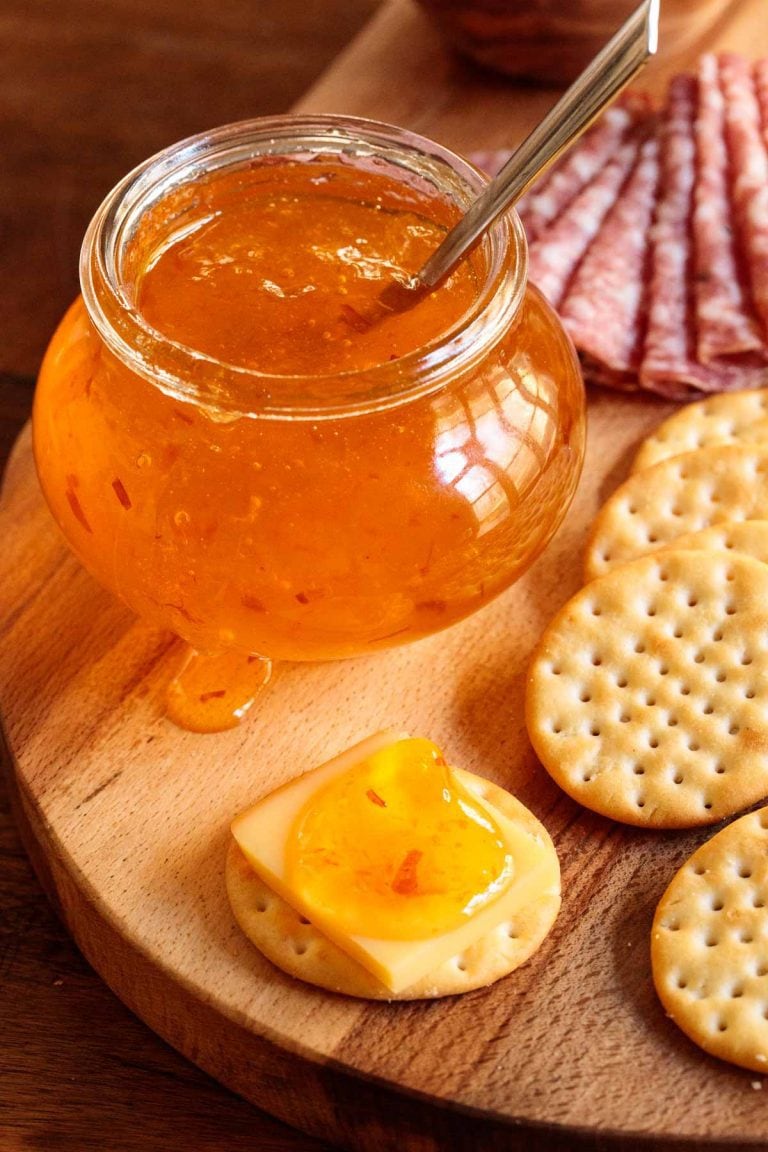 Vertical closeup photo of Clementine Pepper Jelly with cheese and crackers.