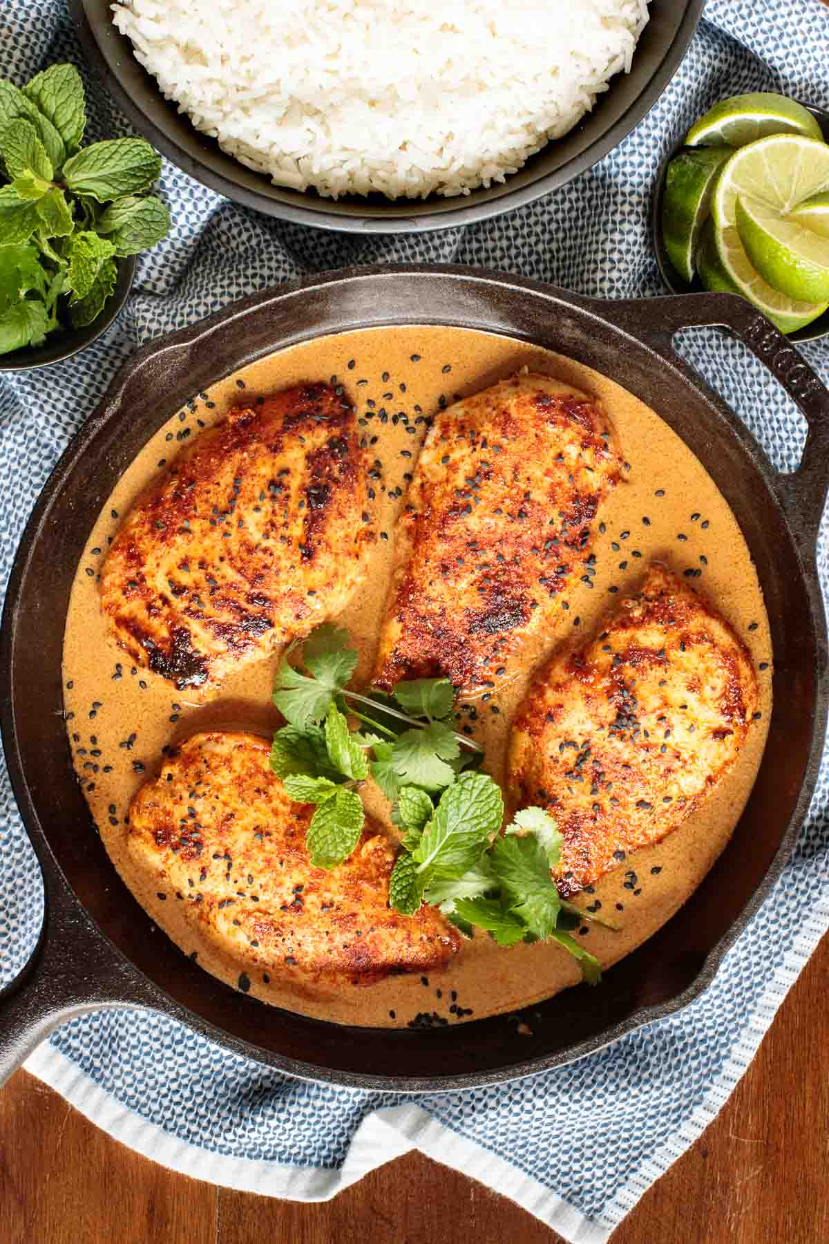 Overhead vertical photo of Coconut Braised Chicken Breasts in a cast iron skillet on a blue and white patterned kitchen towel.