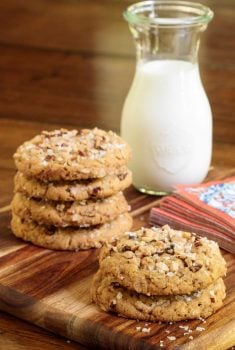 Vertical picture of coconut pecan cookies stacked on a wooden platter with milk