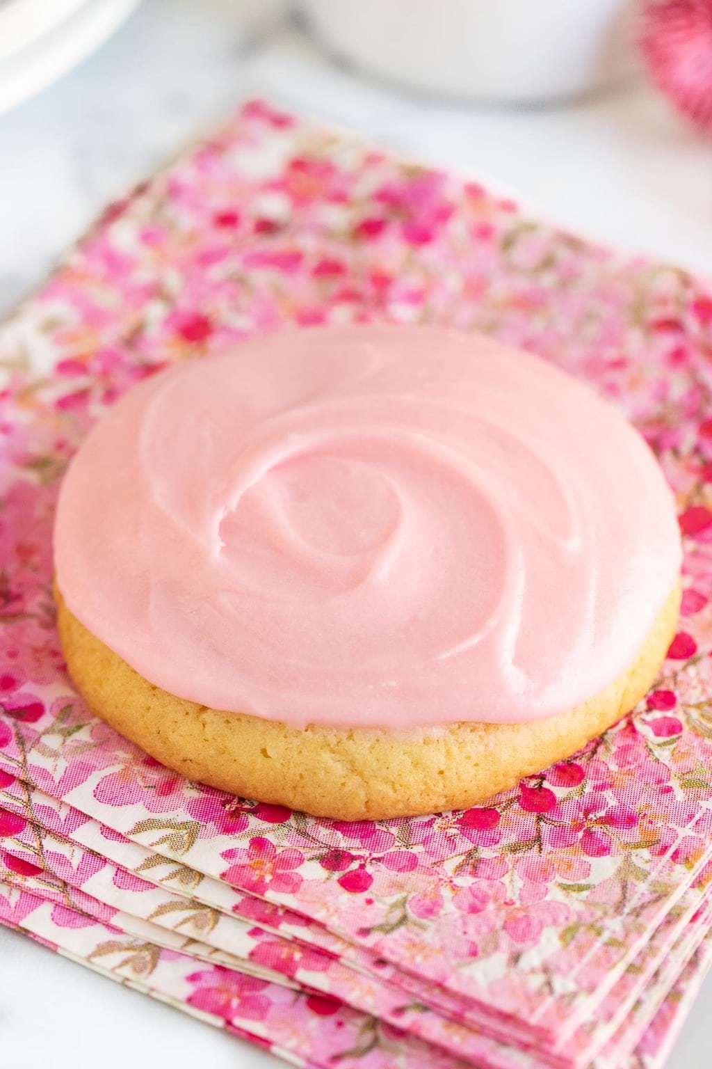 Vertical extreme closeup photo of a Copycat Crumbl Sugar Cookie on a red, pink and white patterned napkin.