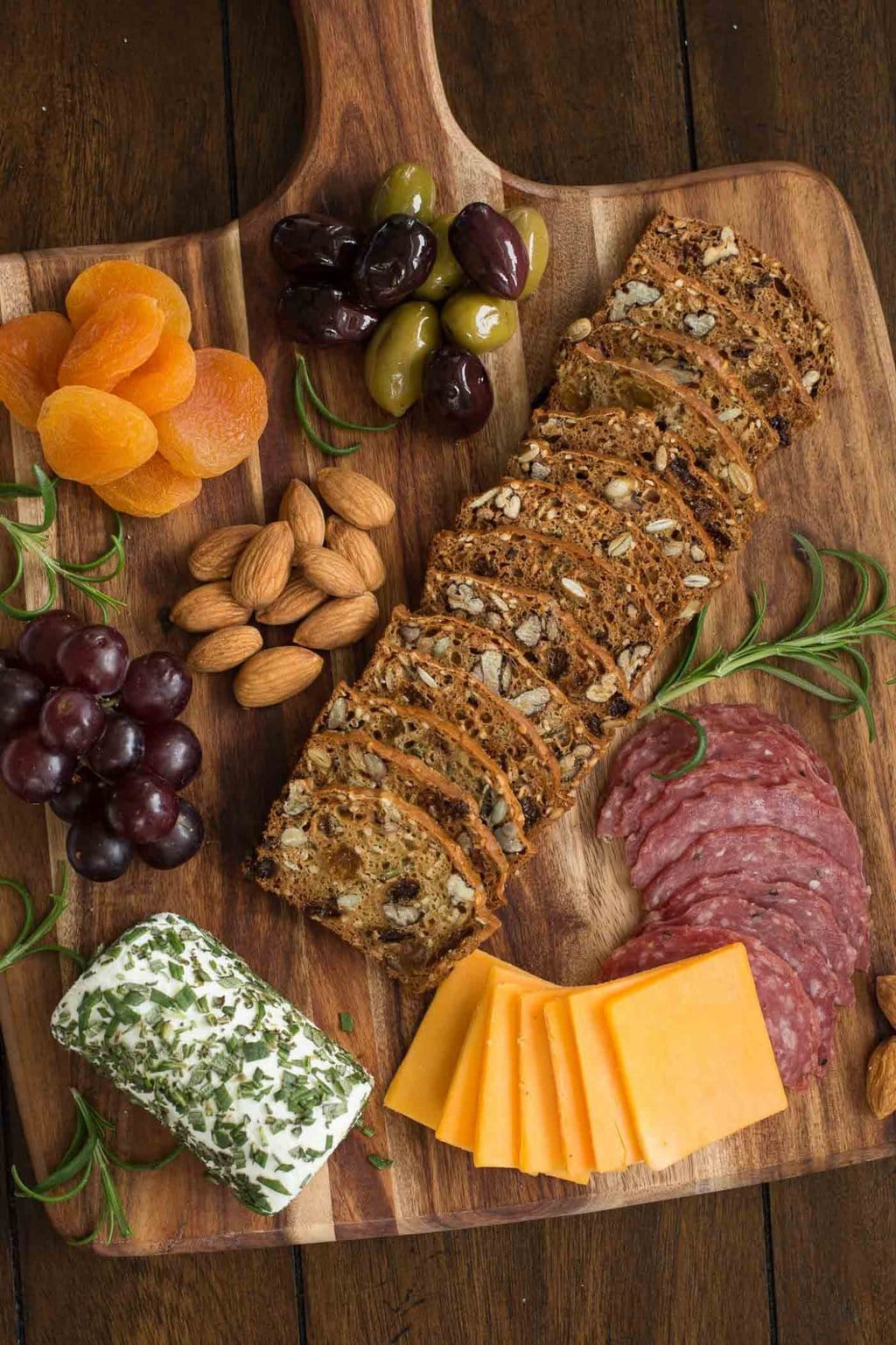 Vertical overhead picture of Rosemary Raisin Pecan Crisp Crackers on a wooden cutting board with cheese and salami