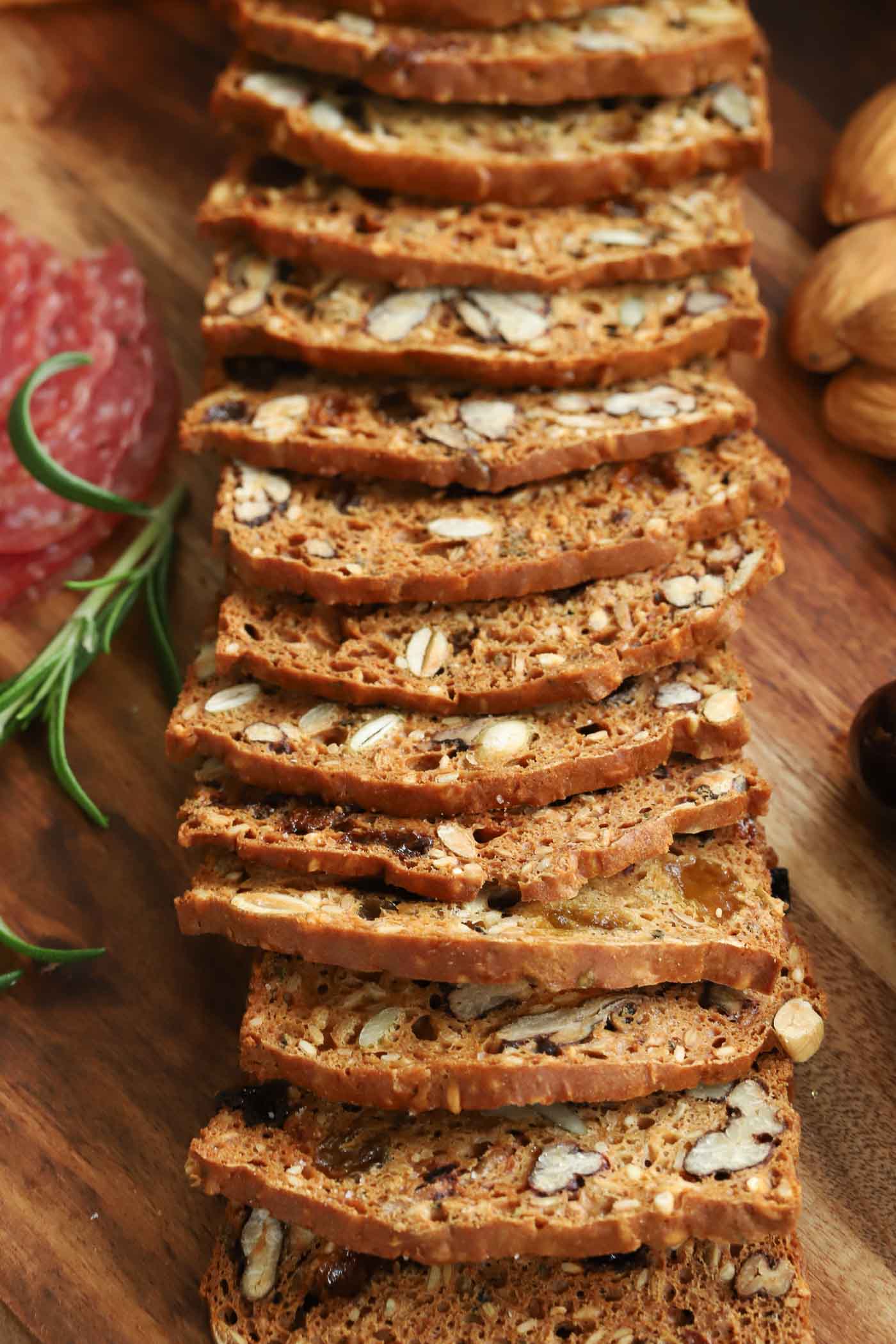 Vertical closeup photo of a row of Copycat Rosemary Pecan Raincoast Crackers on a wooden cheeseboard surrounded by other appetizer snacks.