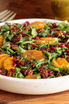 Horizontal photo of a Cranberry Clementine Arugula Salad in a white granite serving bowl.