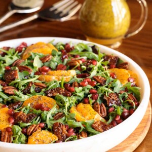 Vertical picture of cranberry clementine salad in a white bowl with a small cruet of dressing in the background