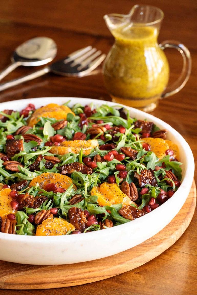 Vertical picture of cranberry clementine salad in a white bowl with a small cruet of dressing in the background