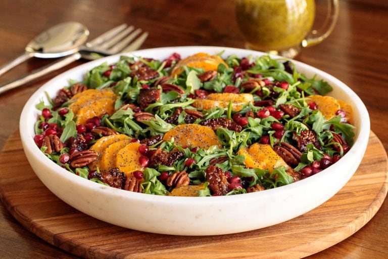 Horizontal photo of a Cranberry Clementine Arugula Salad in a white granite serving bowl.