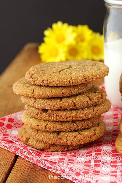 A photo of a stack of Biscoff Toffee Cookies on a red and white napkin on a wood table with a jar of milk and yellow daisies in the background.