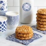 Horizontal photo of a batch of Crispy Chewy Carolina Coconut Cookies with glasses of milk in the background.