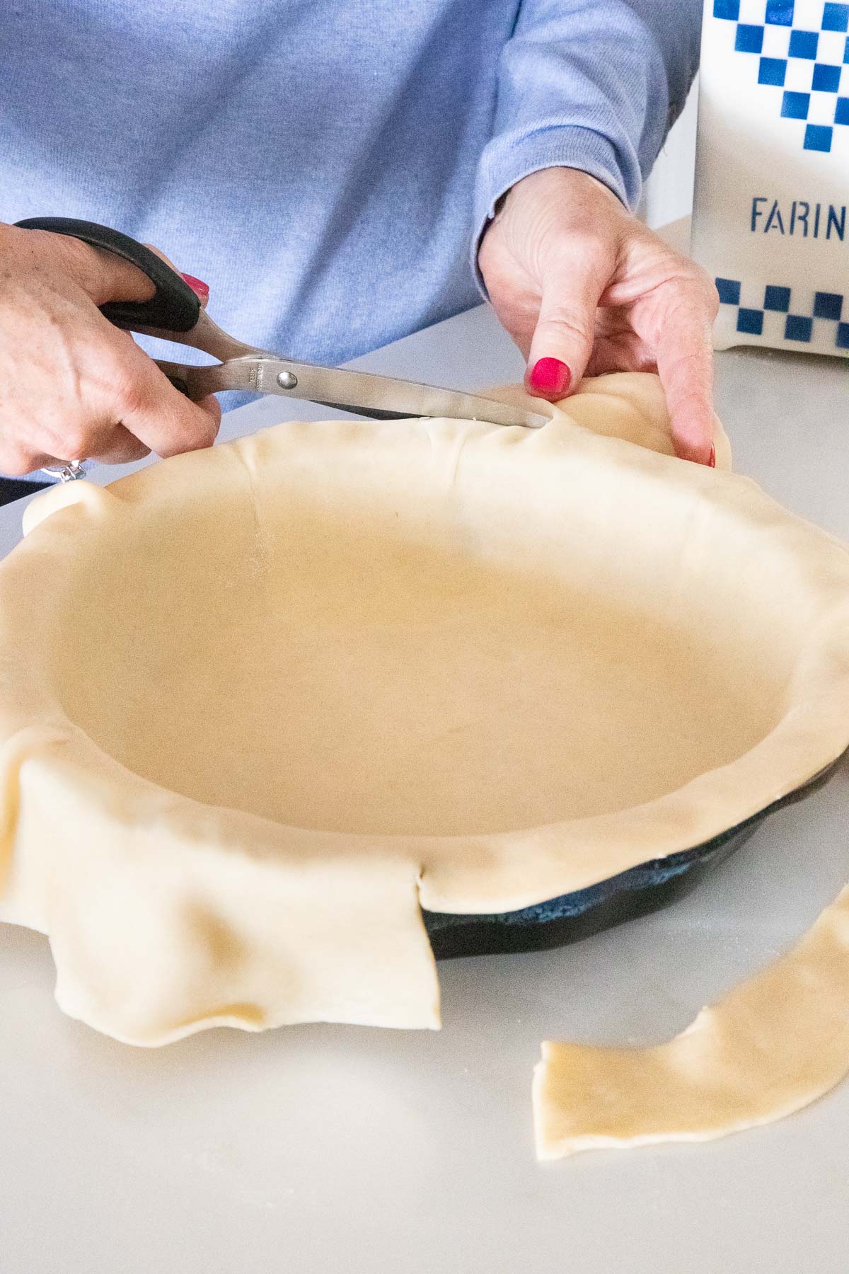 Vertical photo of cutting the excess crust off of a Homemade Store-Bought Pie Crust with scissors.