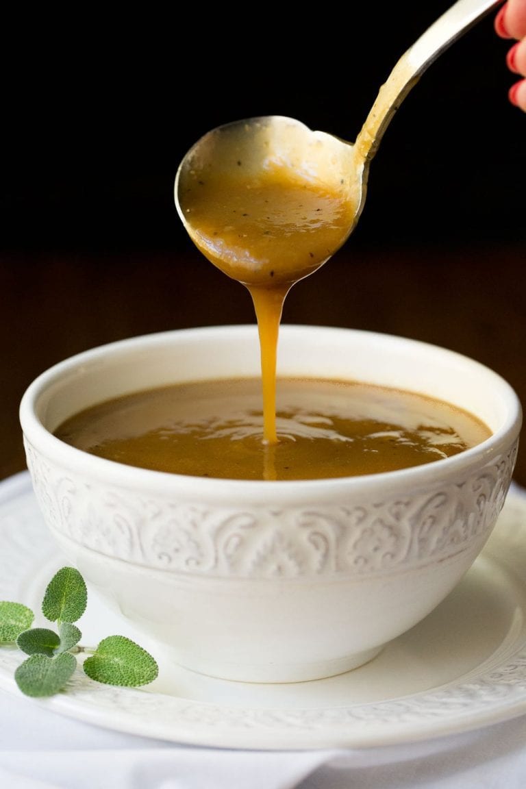Vertical picture of make-ahead gravy in a white bowl with a ladle
