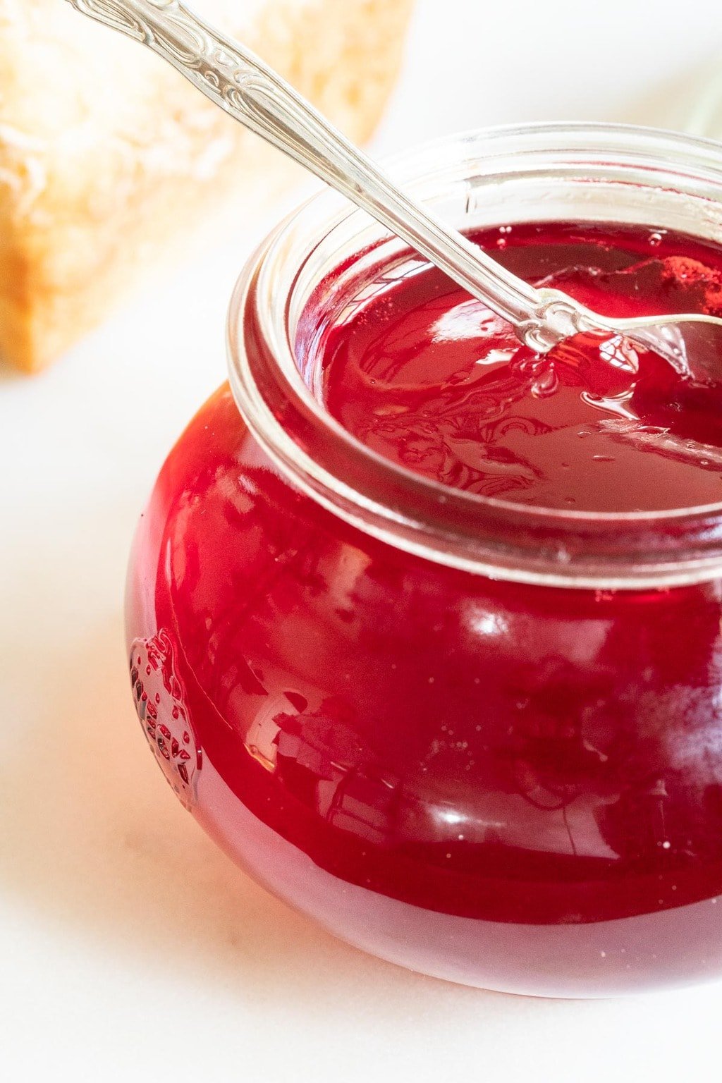 Vertical photo of a jar of Easy Blackberry Jelly with a slice of homemade bread in the background..