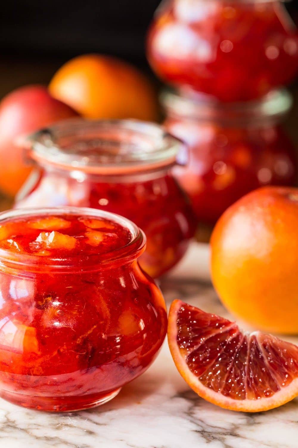 Photo of glass Weck jars of Easy Blood Orange Marmalade surrounded by blood oranges.