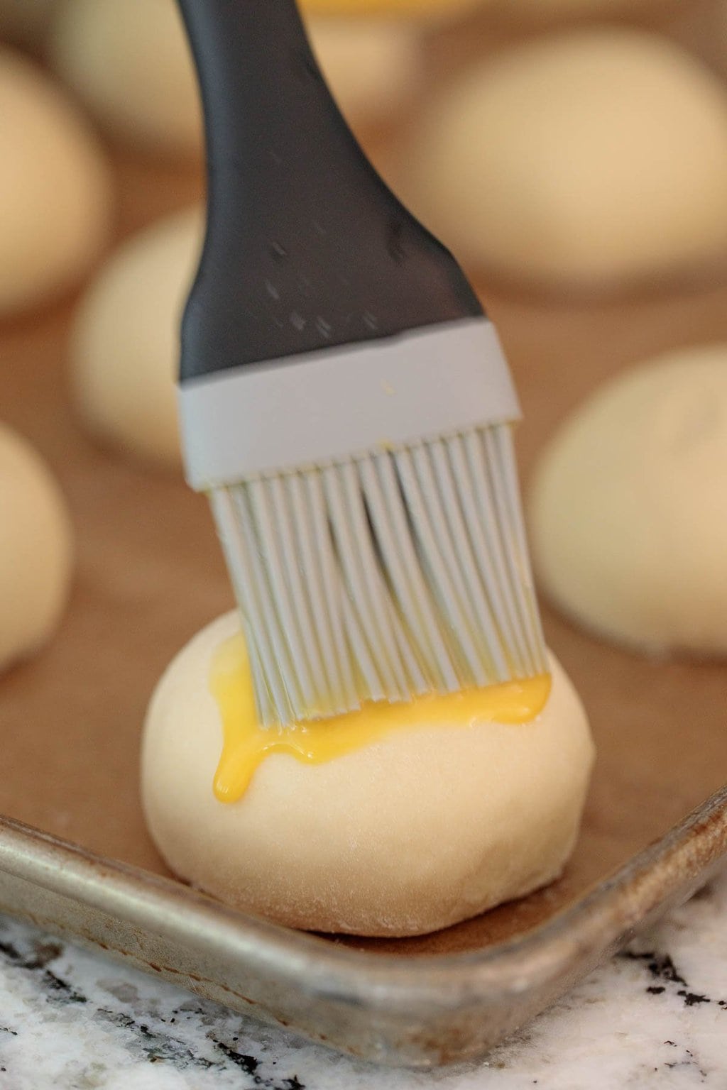 Using a silicone brush to apply the egg coating on a batch of Easy Buttermilk Brioche Buns.