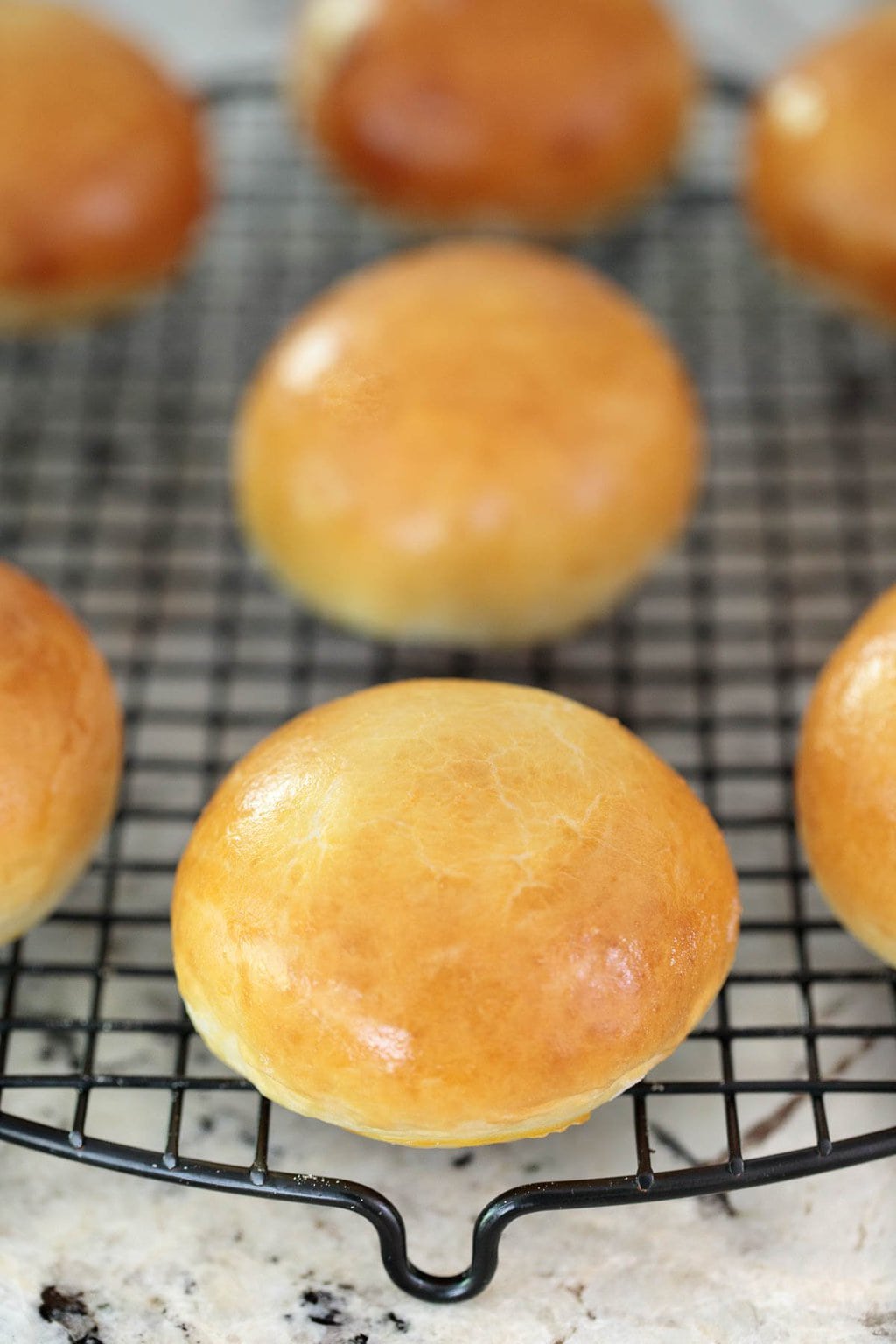 Vertical photo of Buttermilk Brioche Buns resting on a cooling rack.