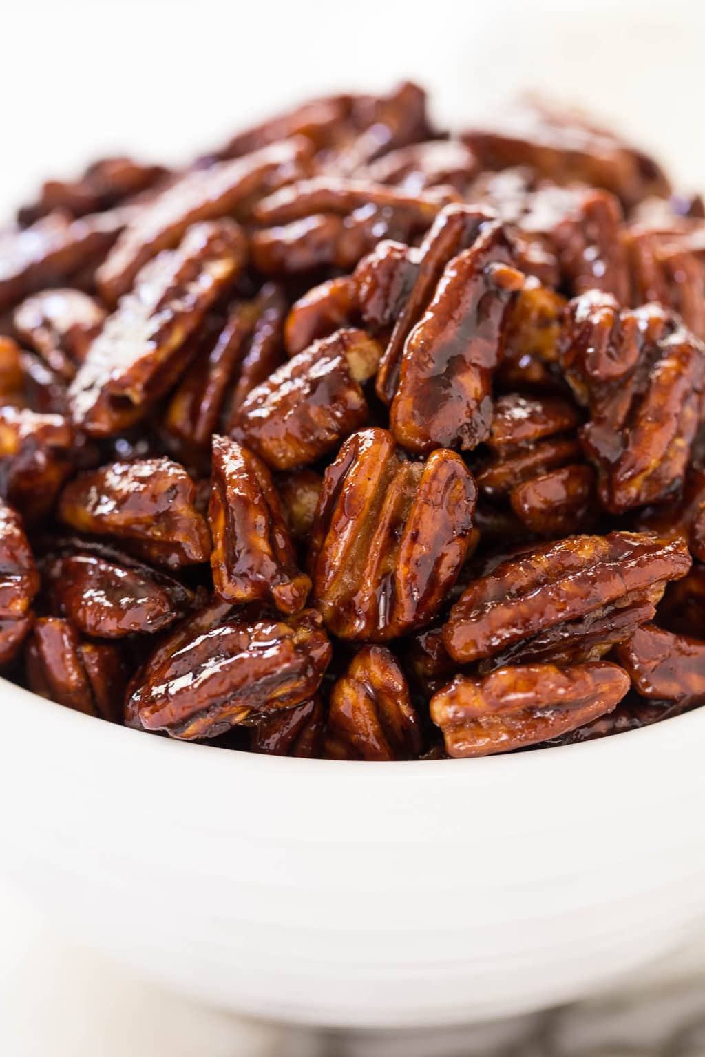 Vertical extreme closeup photo of a white bowl filled with Easy Candied Pecans.