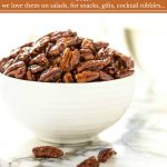 Vertical photo of a white serving bowl filled with Easy Candied Pecans on a round marble surface.