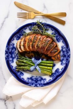 Overhead vertical photo of a plate of Prosciutto-Wrapped Chicken Breasts on a blue plate with grilled asparagus spears as a side.