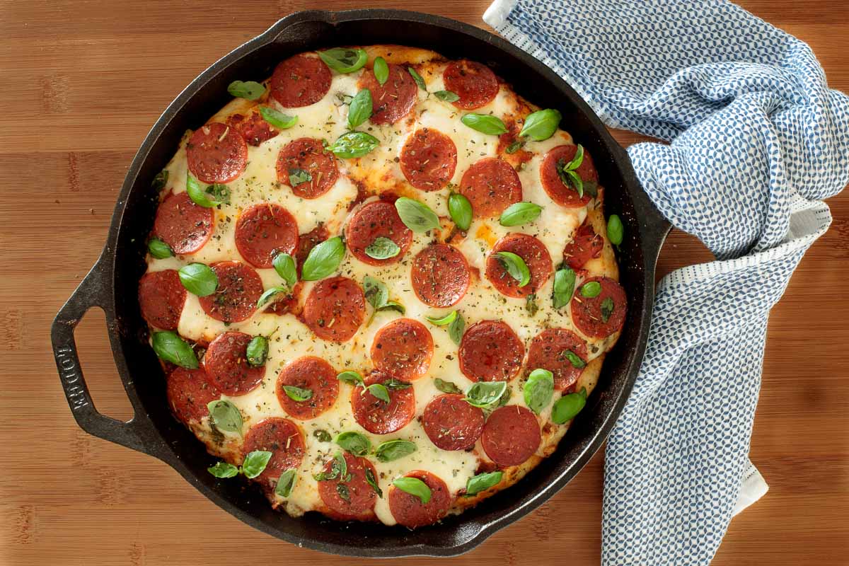 Overhead photo of a fully baked Easy Deep Dish Pizza Dough pizza in a cast iron skillet on a wood cutting board.