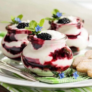 Vertical photo of an Easy Irish Blackberry Fool in small glass jars garnished with mint and small blue flowers.