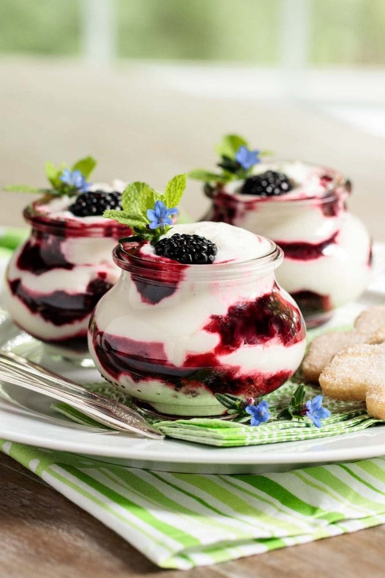 Vertical photo of an Easy Irish Blackberry Fool in small glass jars garnished with mint and small blue flowers.
