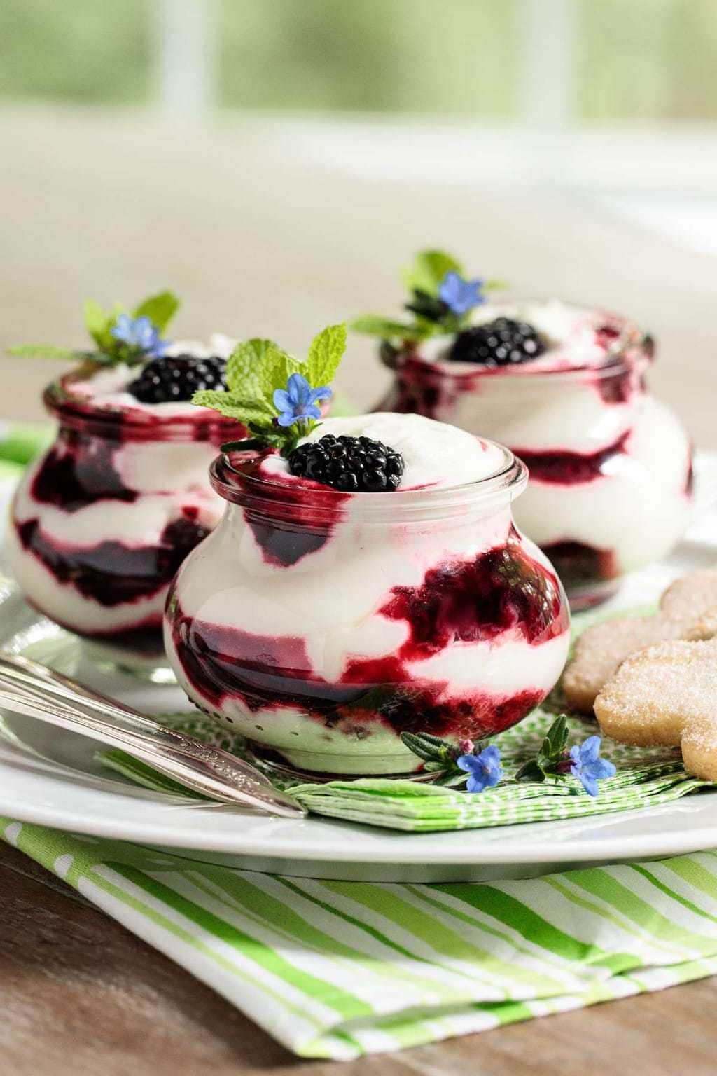 Vertical photo of Easy Irish Blackberry Fool in small glass jars garnished with sprigs of fresh mint and tiny blue flowers.