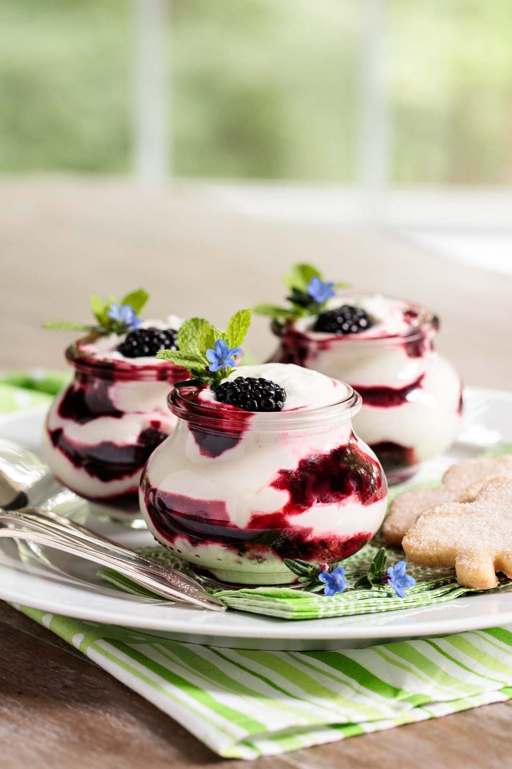 Vertical photo of a serving plate full of Irish Blackberry Fool desserts in individual glass Weck jars on a dining room table.