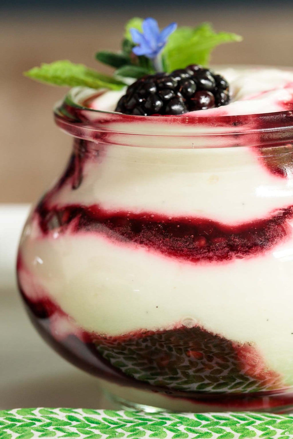 Closeup photo of an Irish Blackberry Fool in a clear glass Weck jar garnished with mint and wildflowers.