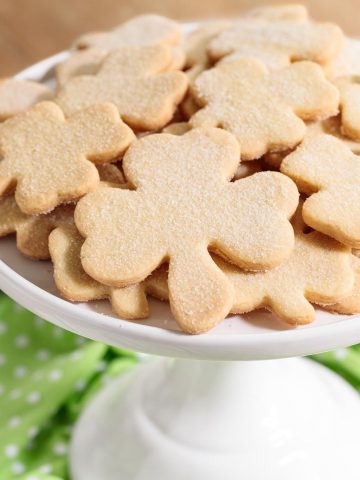 Vertical photo of Easy Irish Shortbread shamrock cookies on a white cake stand.