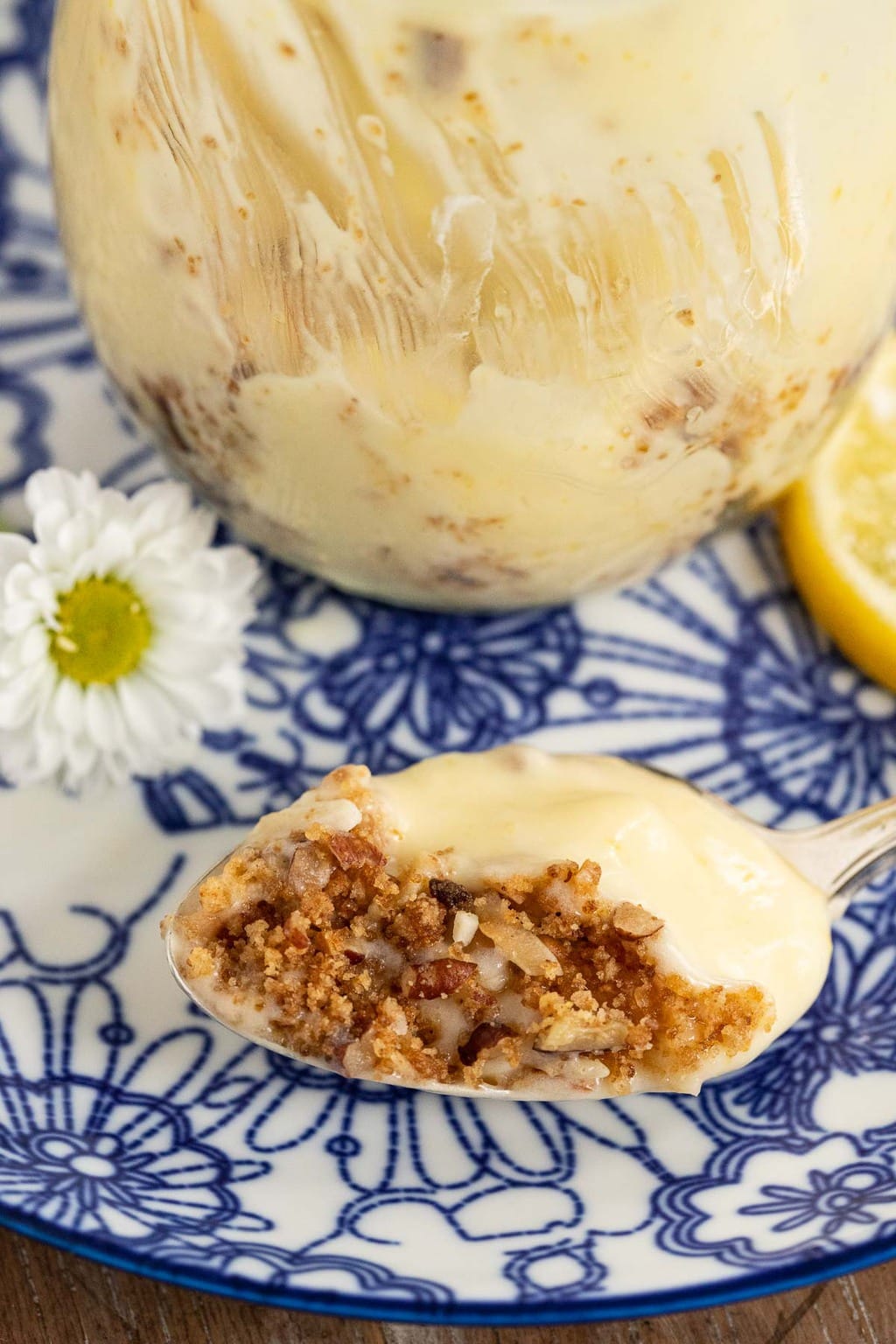 Closeup of a spoonful of Easy Lemon Curd Mousse in front of a jar of the same on a blue and white patterned plate.