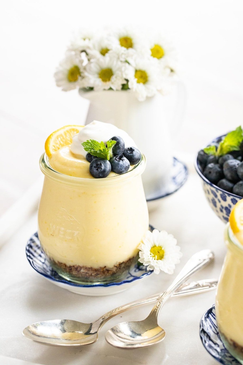 Vertical photo of a glass dessert jar of Easy Lemon Curd Mousse garnished with fresh blueberries and mint leaves.