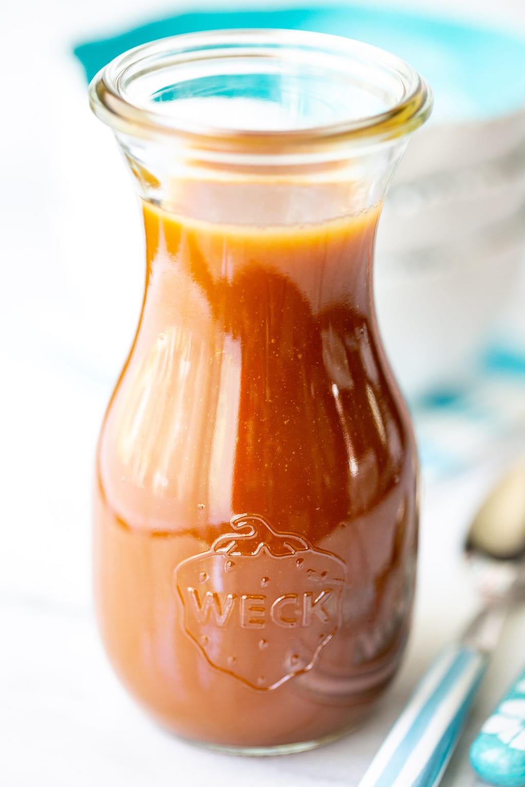 Vertical closeup photo of a glass carafe filled with Easy Microwave Caramel Sauce.
