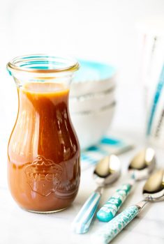 Vertical picture of easy Microwave Caramel Sauce in a glass jar with blue and white bowls