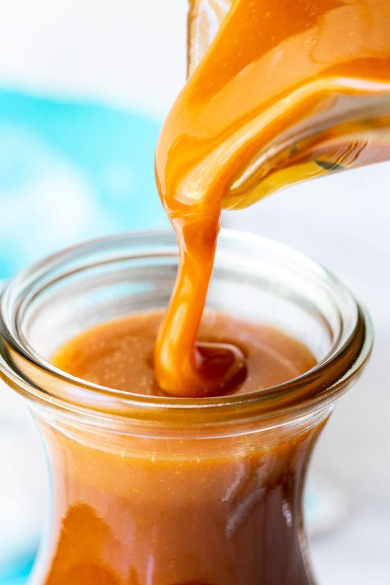 Vertical extreme closeup of Easy Microwave Caramel Sauce being poured into a glass carafe.