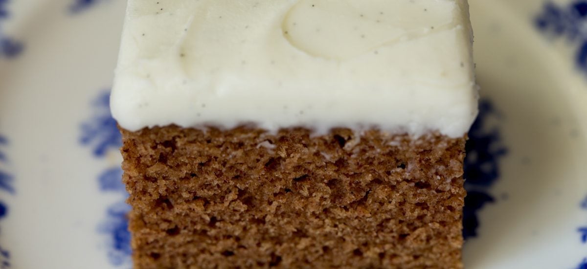 Side photo of a piece of Easy Gingerbread Cake with Vanilla Bean Icing on a delft blue patterned plate.