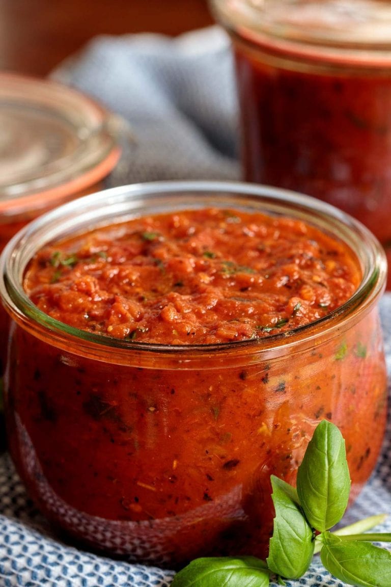 Vertical picture of easy pizza sauce in a glass jar with a basil garnish